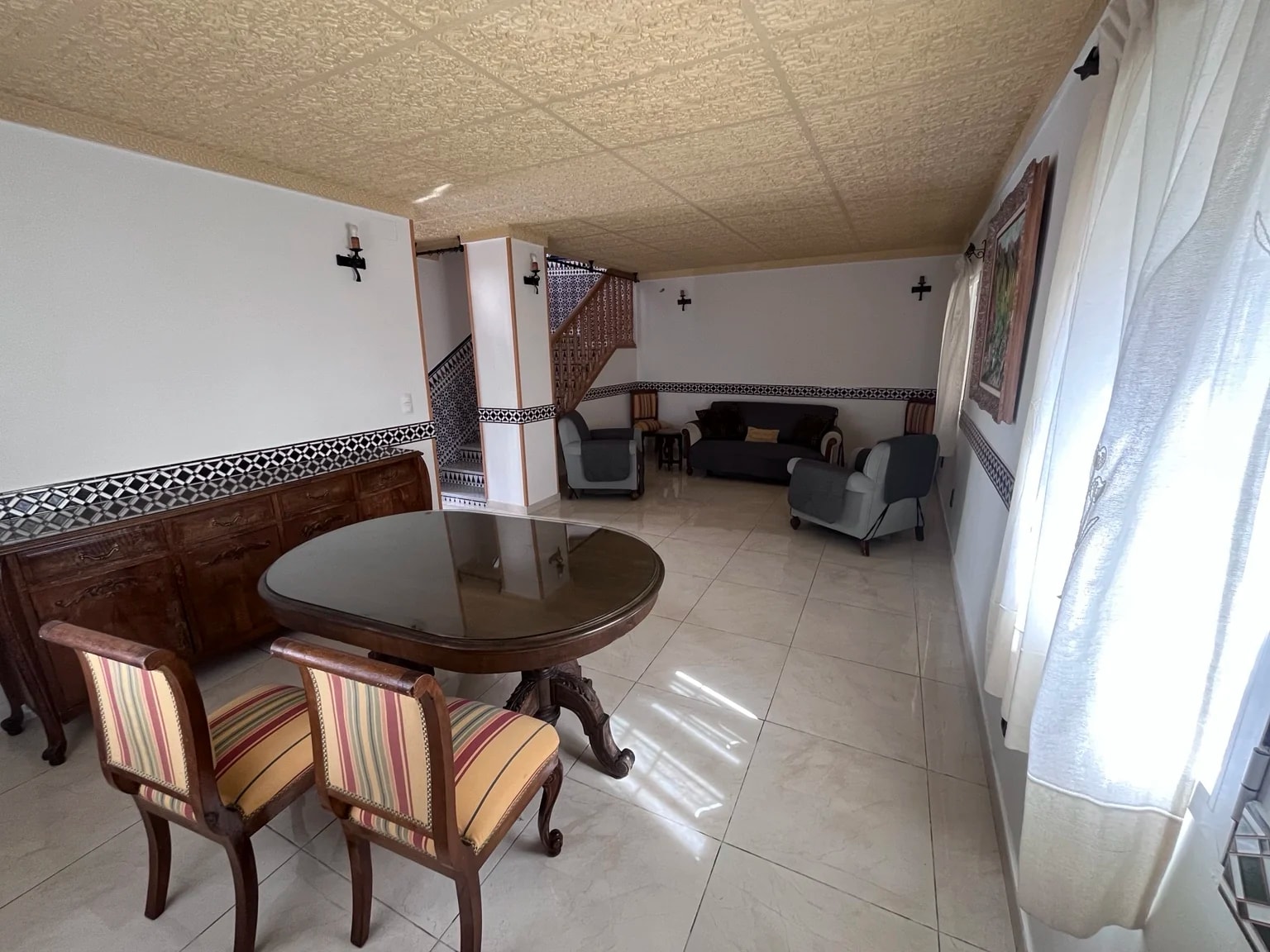 Salón comedor de la casa, con mesa redonda, sillas, sofás y ventanales.